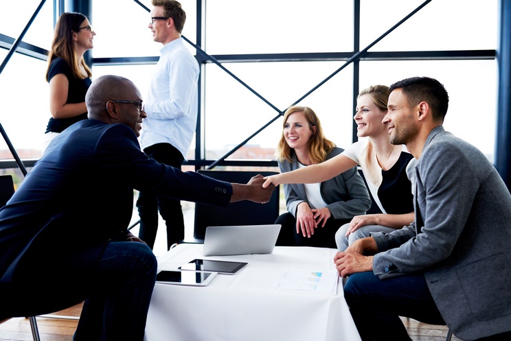 Black male executive sitting and shaking hands with white female colleague